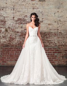 a woman in a white wedding dress standing next to a brick wall with her hands on her hips