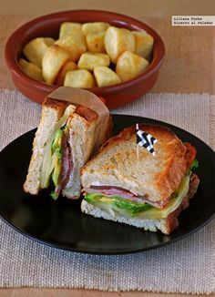 a black plate topped with a cut in half sandwich next to a bowl of potatoes