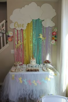 a table topped with cake and cupcakes under a rainbow curtain