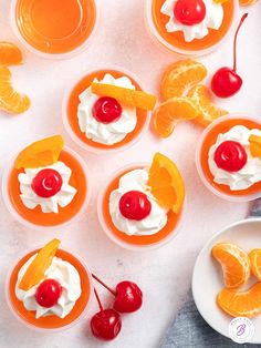 oranges and cherries are garnished with whipped cream in small bowls on a white surface