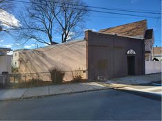 an empty street in front of a building with a fence and trees on the side