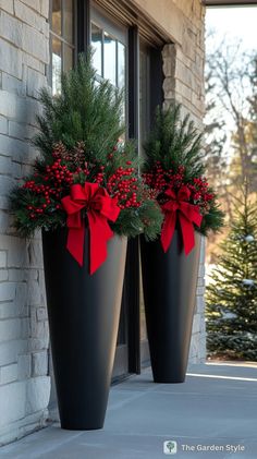 two large black vases with red bows on the front of a building, decorated for christmas