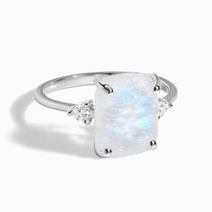 a white ring with an opal stone and three diamonds on the side, set in 18k white gold