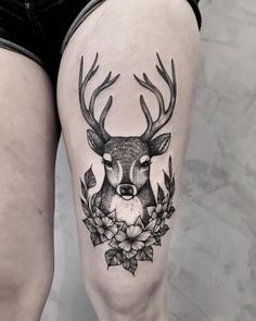 a woman's thigh with a deer and flowers tattoo on her leg, which is decorated with leaves