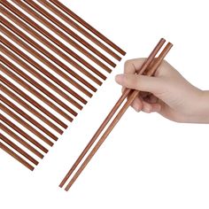 a hand holding chopsticks next to a stack of wooden dowels on a white background