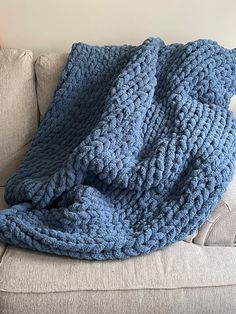 a blue crocheted blanket sitting on top of a couch next to a pillow