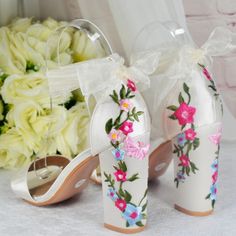 a pair of white high heeled shoes with flowers painted on them and bows tied to the heels