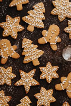 some cookies with white icing and snowflakes are on a black surface next to a spoon