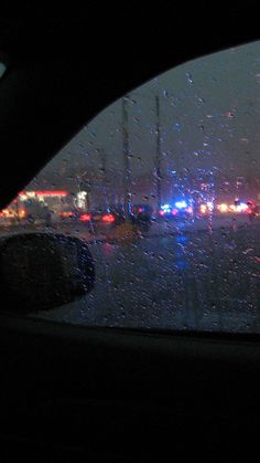 rain is falling on the windshield of a car as traffic passes through an intersection at night