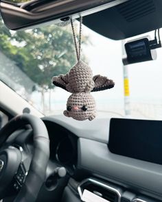 a crocheted stuffed animal hanging from the dashboard of a car with steering wheel