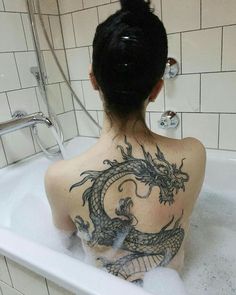 a woman with a dragon tattoo on her back sitting in a bathtub filled with water