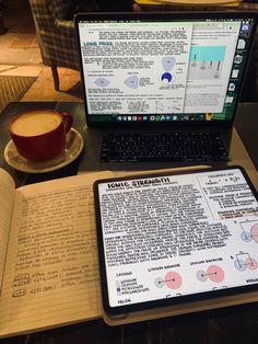 an open book sitting on top of a table next to a laptop computer and cup of coffee