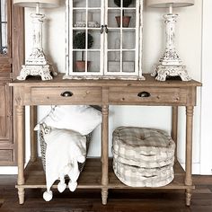 a wooden table topped with two lamps next to a shelf filled with pillows and blankets