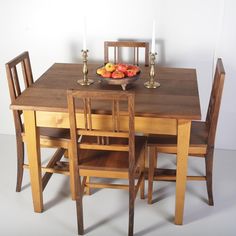 a bowl of fruit sitting on top of a wooden table with four chairs around it