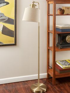 a floor lamp next to a book shelf with books on it and a painting in the background