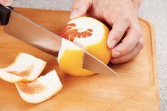 a person cutting an orange with a knife on a cutting board next to some cut up pieces