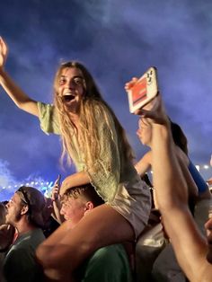 a woman is holding up her cell phone in the air as she sings at an outdoor concert