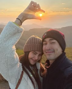 a man and woman taking a selfie with the sun setting in the back ground