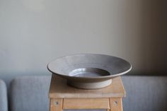 a white bowl sitting on top of a wooden stool in front of a gray couch