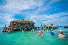 people are swimming in the ocean near a hut on stilts that is built into the water