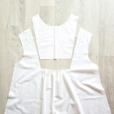 a white dress laying on top of a wooden floor next to a pair of scissors