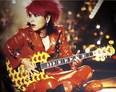 a woman with red hair playing an electric guitar in front of a city at night