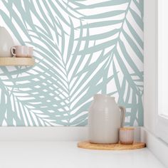 a white vase sitting on top of a counter next to a wall with palm leaves painted on it