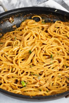 a skillet filled with noodles and sauce on top of a white cloth covered table