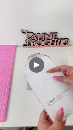 a person is cutting out some paper on top of a white table with pink trimmings