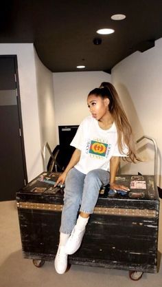 a young woman sitting on top of an old suitcase in a room with white walls