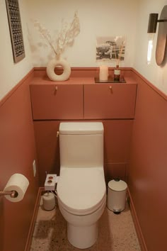 a toilet in a small bathroom with pink walls and flooring, along with two rolls of toilet paper