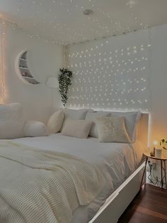 a bedroom with white bedding and lights on the wall, along with a round window