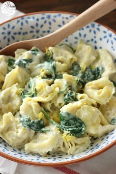 a pasta dish with spinach and cheese in a blue and white bowl on a table