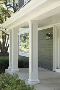 the front porch is covered with white pillars and columns that are lined up against the house's gray siding