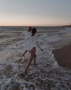 two girls are playing in the water at the beach while one girl is wearing a white dress