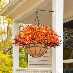 a hanging planter filled with orange flowers on a porch next to a white house