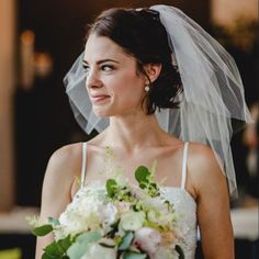 a woman in a wedding dress holding a bouquet and looking off to the side with a veil over her head