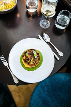 a plate with some food on it next to silverware and wine glasses at a table