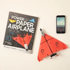 the power up paper airplane book is next to an orange origami plane and cell phone