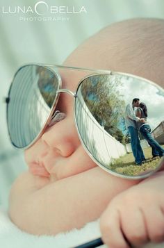 an image of a baby wearing sunglasses with the reflection of his mother and father in them