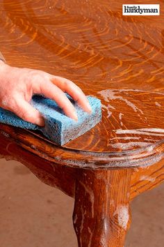 a hand with a sponge on top of a wooden table that has been stained brown