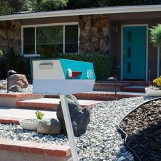 a mailbox in front of a house with rocks and gravel around it, next to a rock garden