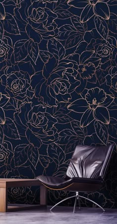 a black chair sitting in front of a wall with gold flowers and leaves on it