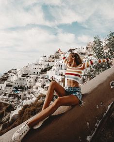 a woman sitting on the edge of a wall talking on a cell phone while wearing shorts