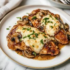 a white plate topped with meat covered in sauce and mushrooms next to silverware on a marble table