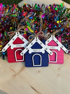 three dog houses with name tags on them sitting in front of tinsel and confetti