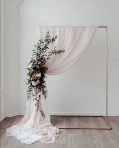 a wedding arch decorated with flowers and greenery on the floor in front of a white wall