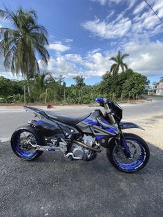 a blue and black motorcycle parked on the side of the road next to palm trees