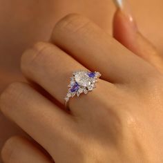 With every glance at our Dahlia Moissanite Tanzanite Ring, may you be reminded of the extraordinary love that blossoms between you. This work of art showcases an oval moissanite, embraced by tanzanite gemstones on each side and surrounded by leafy patterns adorned with sparkling moissanite, adding a whimsical and elegant touch. Let your love story unfold like the petals of a dahlia, revealing its timeless beauty. ✦ Available in 10K/14K Solid White, Yellow, and Rose Gold Tanzanite Engagement Ring Silver, Tanzanite Rings, Tanzanite Engagement Ring, Oval Moissanite, Tanzanite Ring, Tanzanite Gemstone, Gemstone Engagement, Shiny Things, Future Plans