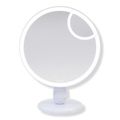 a white round mirror on a stand with a circular light in the middle and an oval shape around it